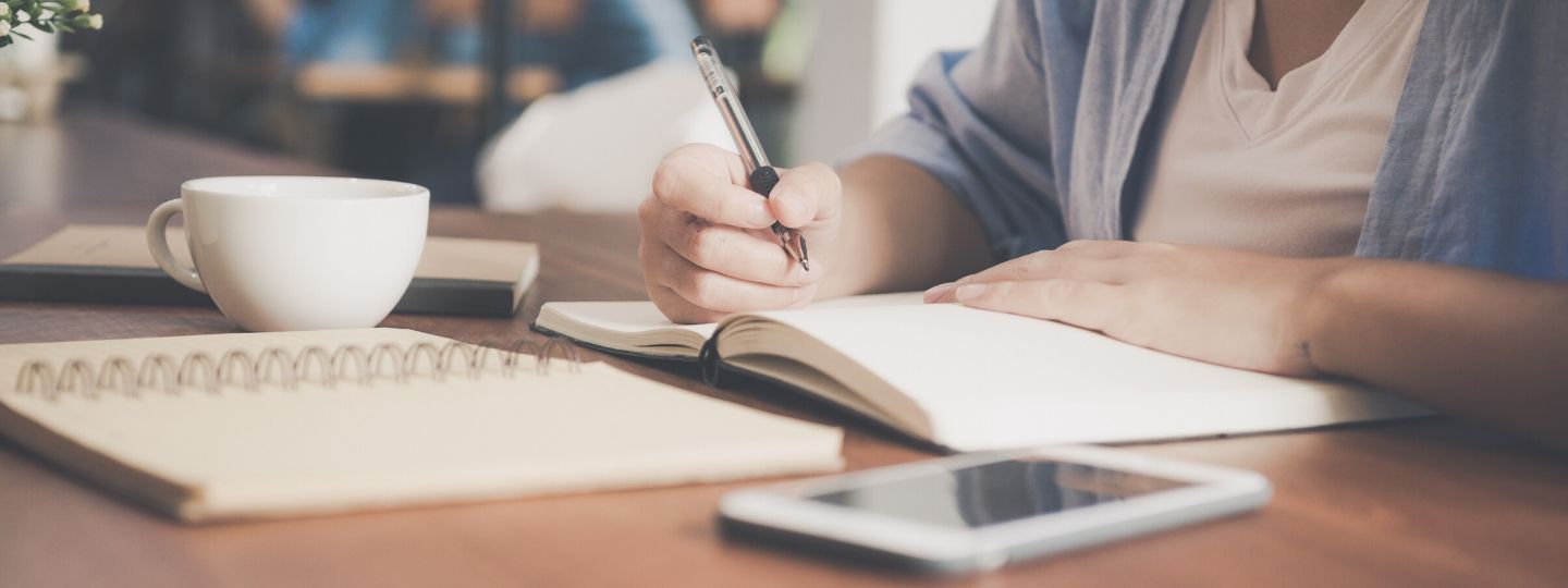 Featured image of person in coffee shop with numerous notebooks and phone to the side on the table